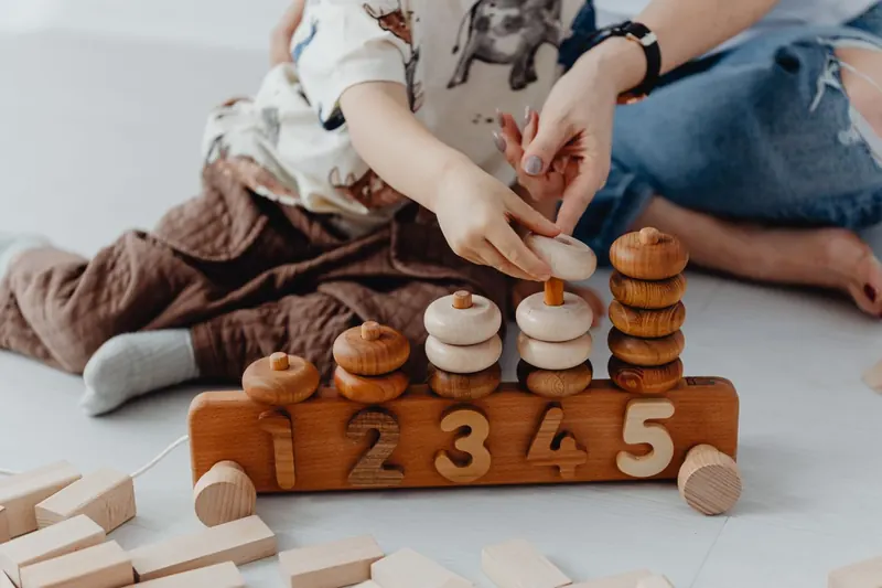 Mains d'un adulte et d'un enfant autour d'un jeu de chiffres en bois